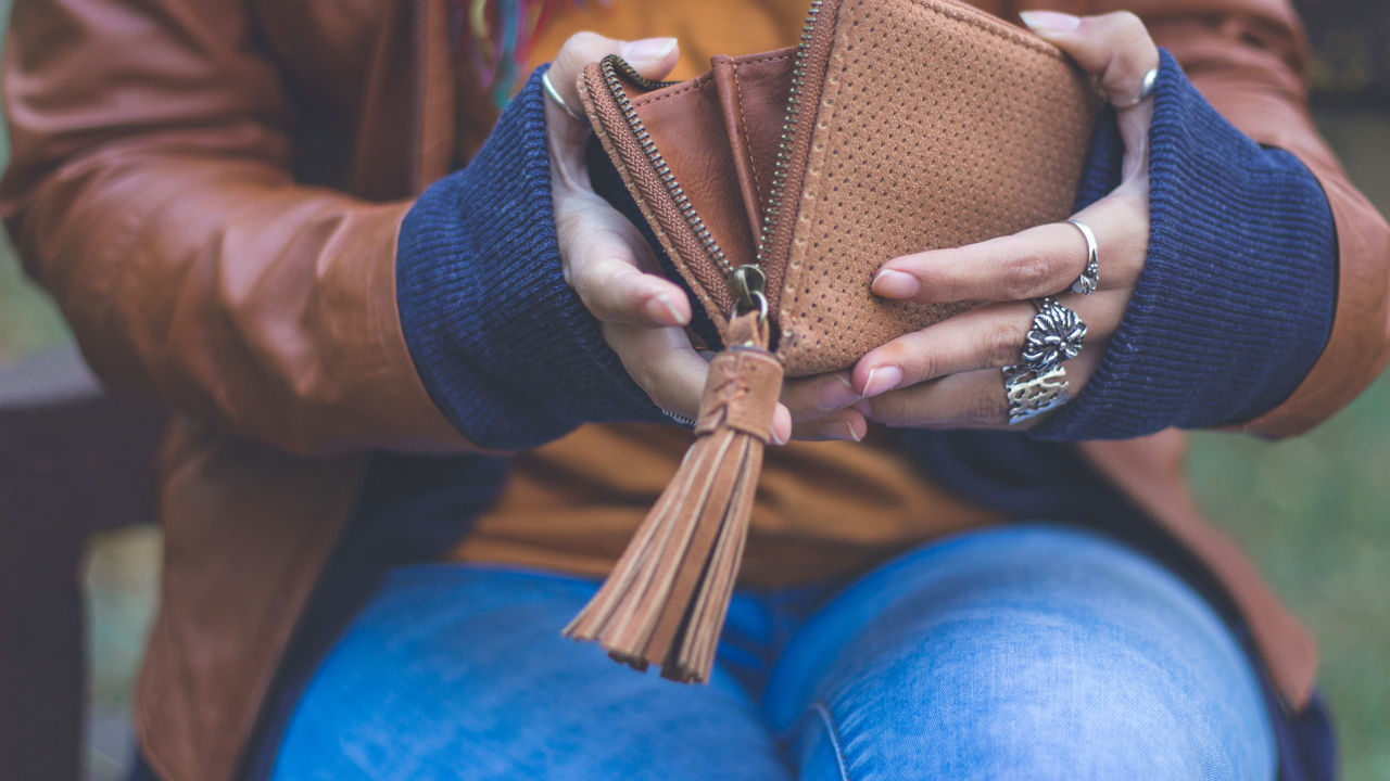 A woman holding a brown wallet with a tassel.