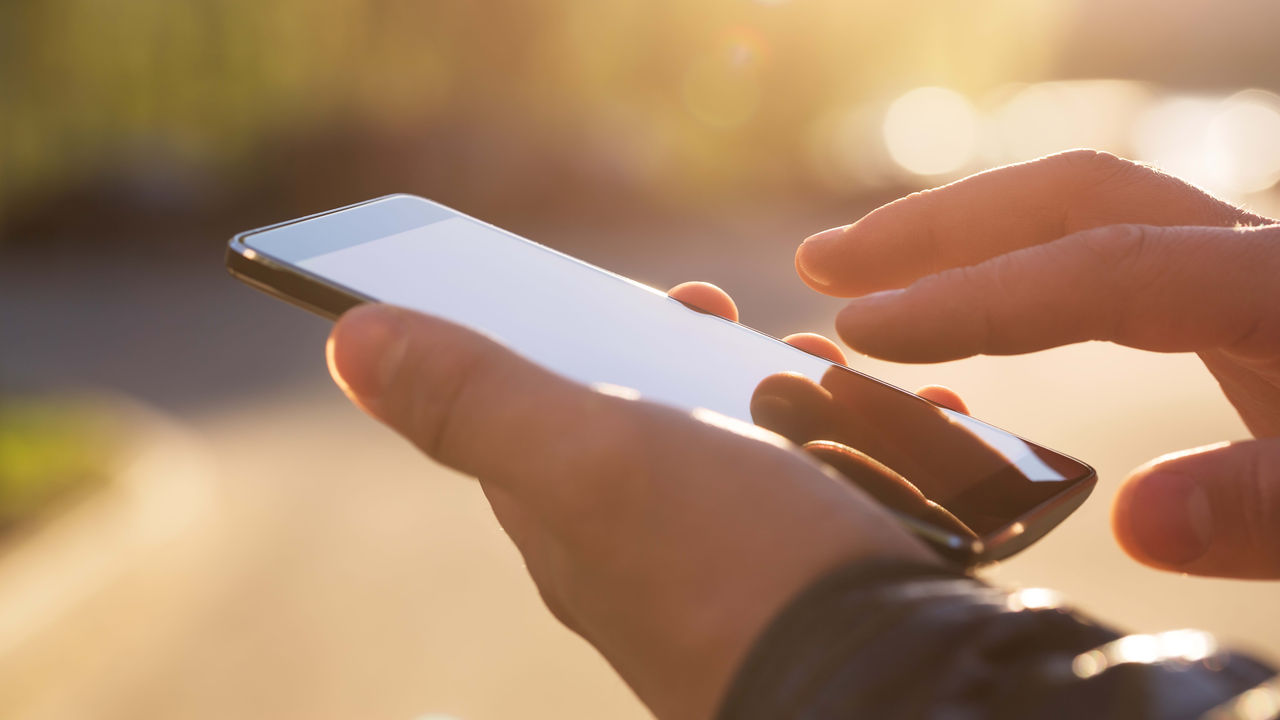 A person holding a smartphone in the sunlight.