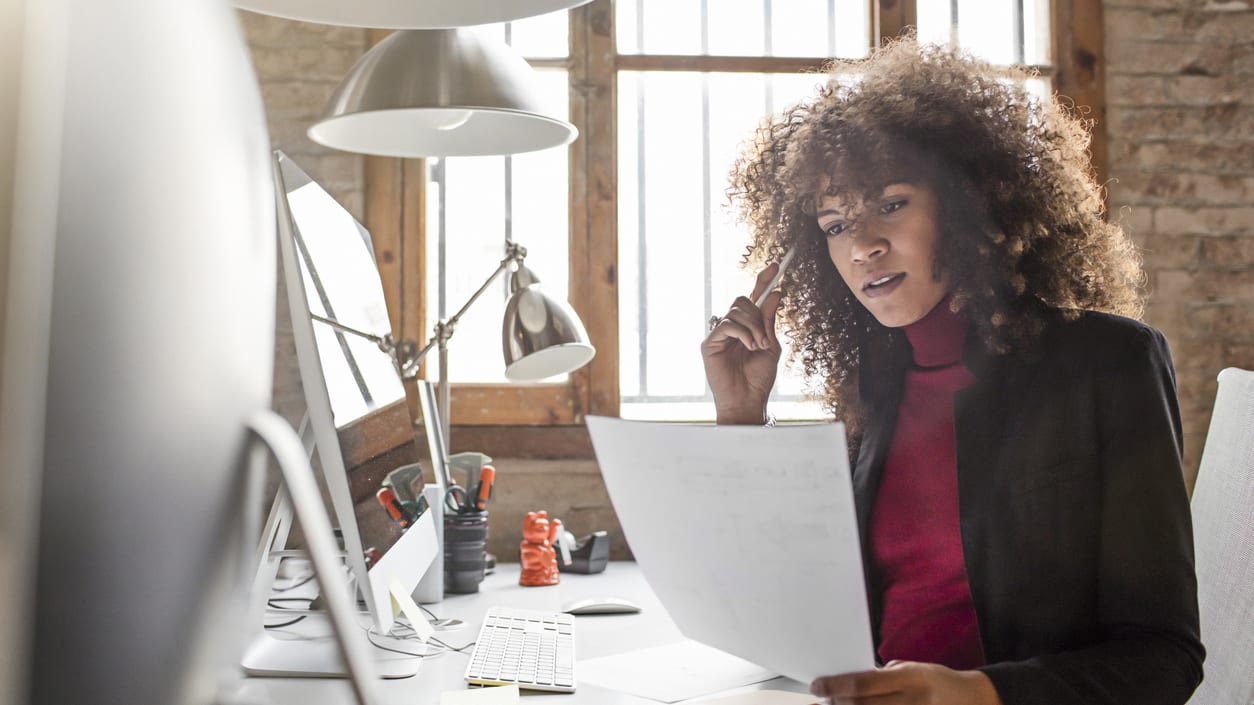 A woman is sitting at a desk looking at a piece of paper.