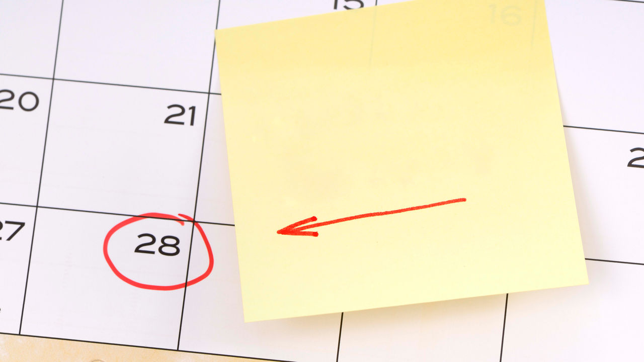 A sticky note with a red arrow on it is on a calendar.