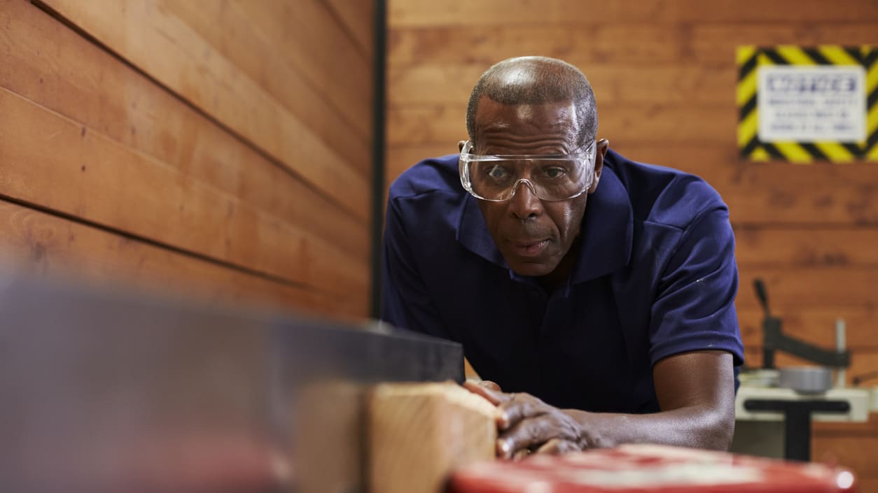 A man in glasses is working on a piece of wood.