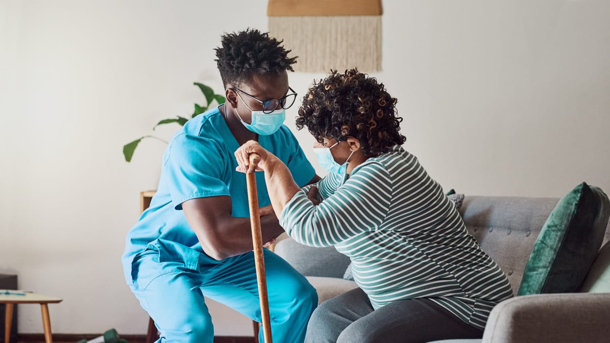 A nurse helping a woman with a cane in the living room.