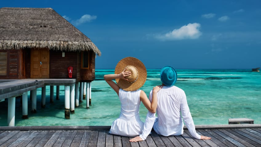 Two people sitting on a dock looking at the ocean.