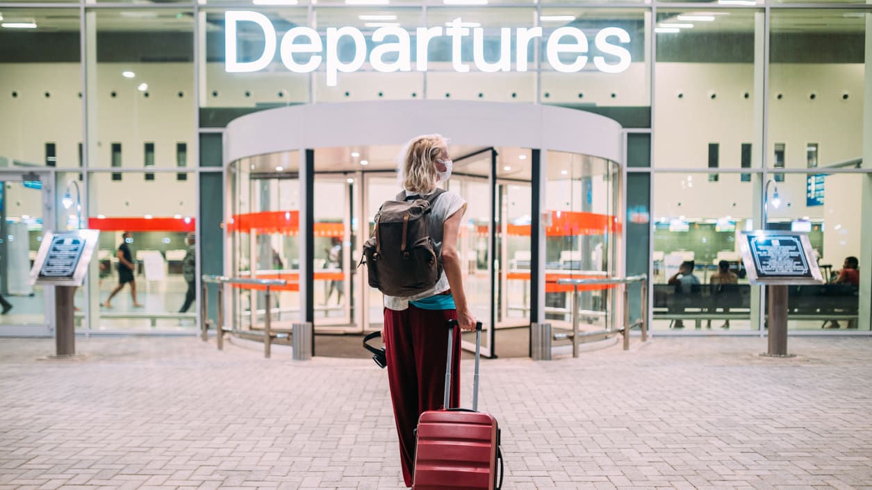 A woman with a red suitcase standing in front of a departures sign.