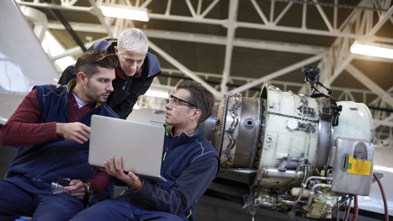 Three men looking at a laptop in a factory.