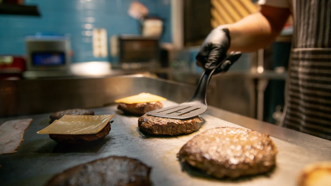 A man is preparing burgers in a kitchen.