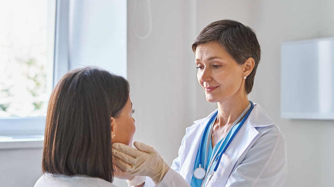 A female doctor is examining a patient's neck.