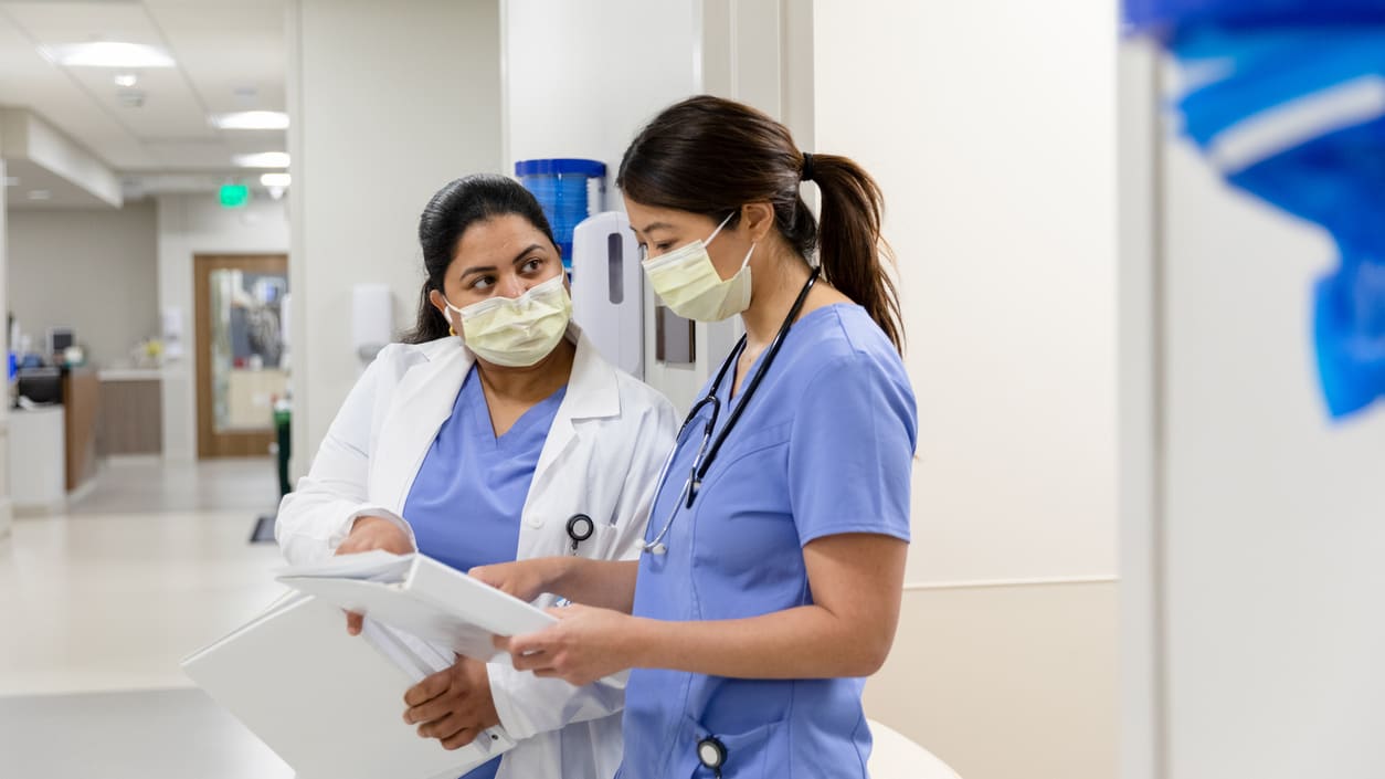 Two nurses in scrubs talking in a hallway.