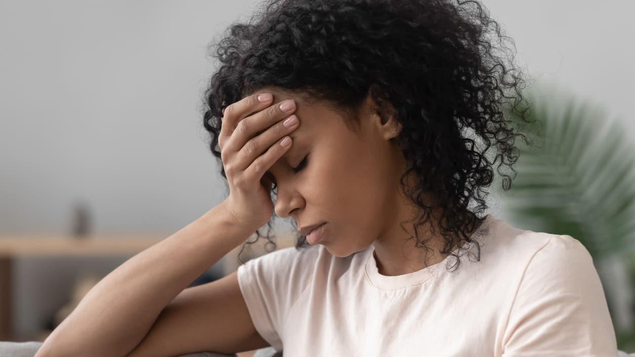 A woman is sitting on a couch with her hand on her head.