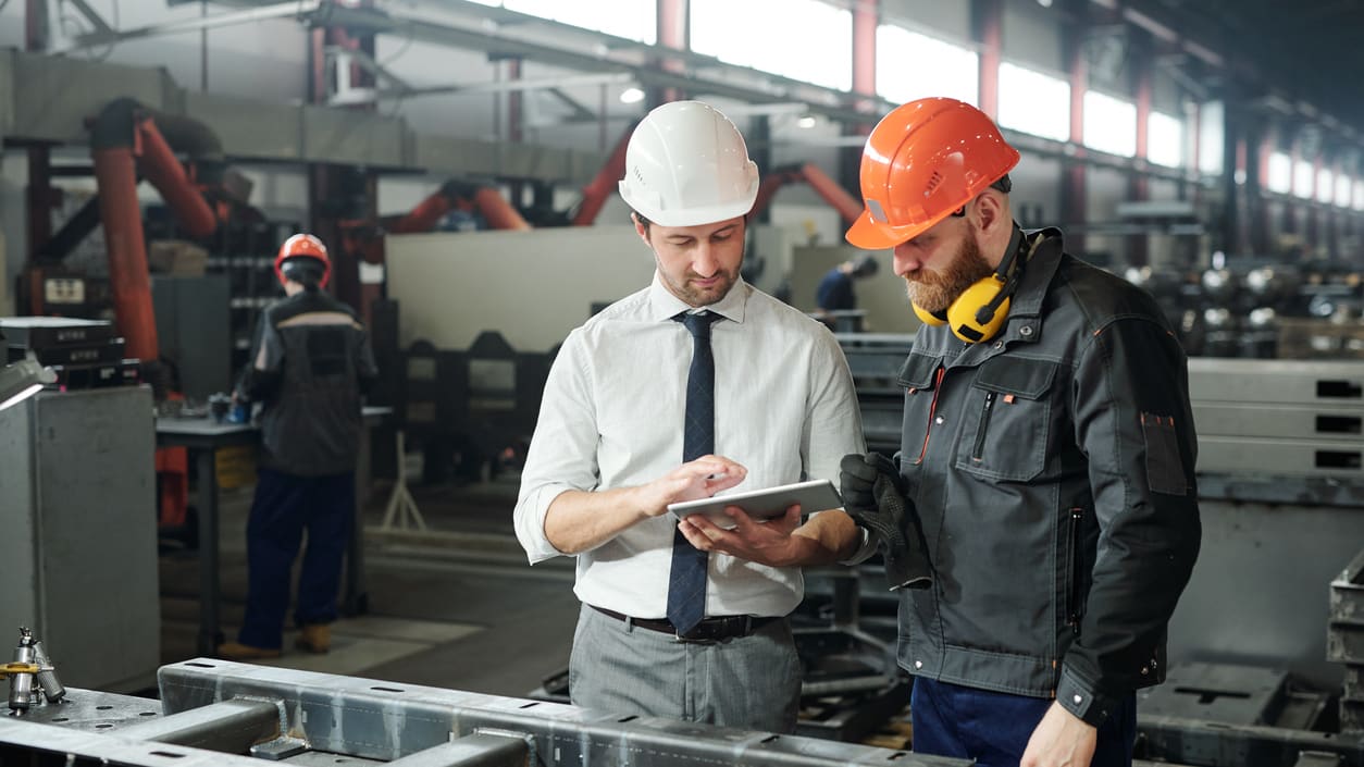 Two men in hard hats looking at a tablet in a factory.