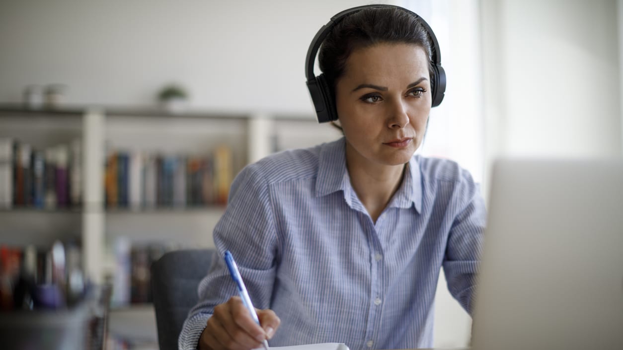 A woman is sitting at a desk with headphones on and a laptop.