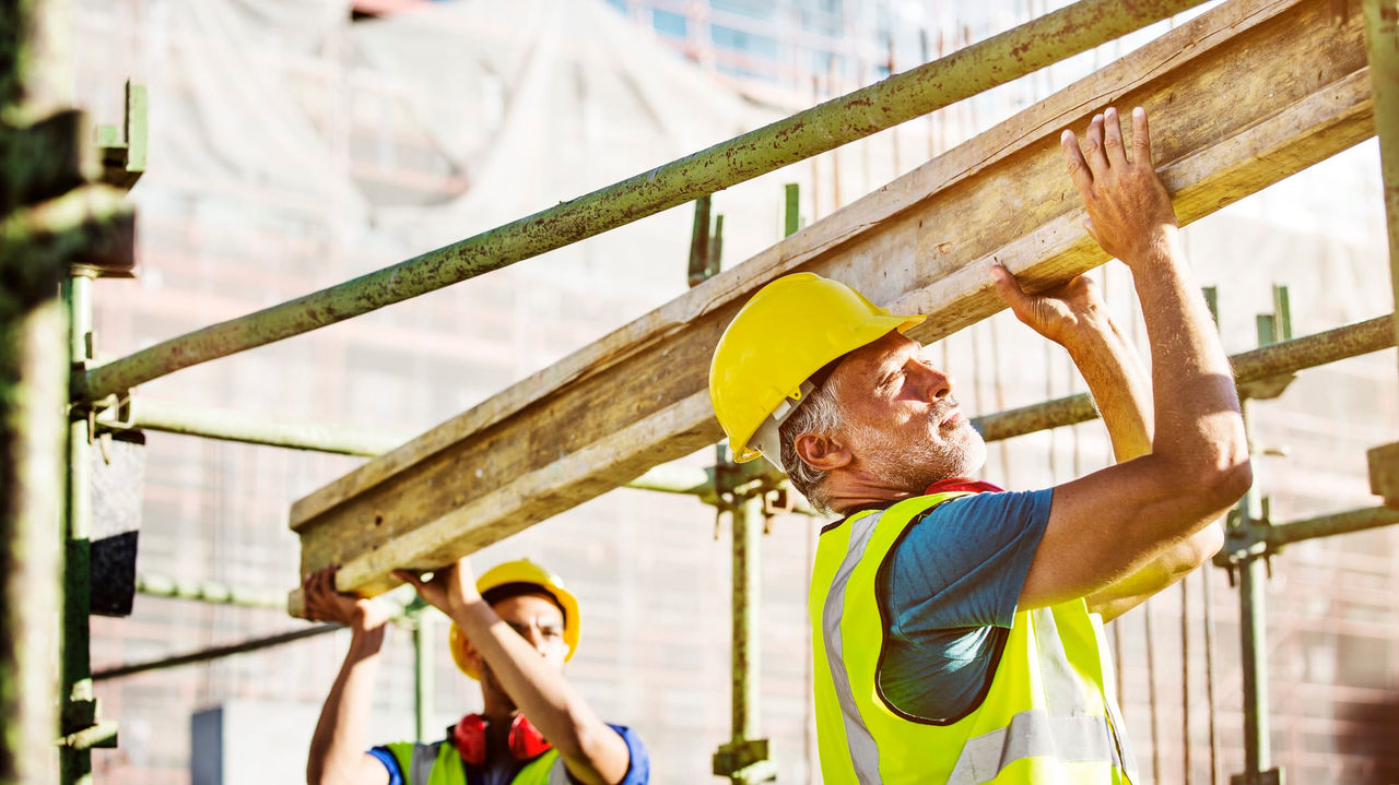 Two construction workers working on a wooden beam.