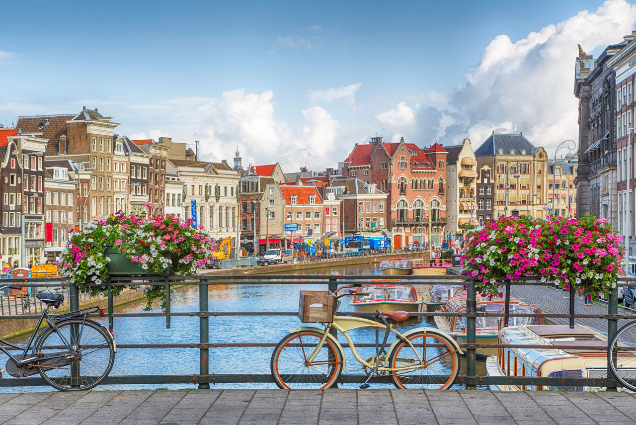Amsterdam, capital of the Netherlands, with a bridge over one of its canals and a bike leaning against the bridge rail with two flower boxes on the rail