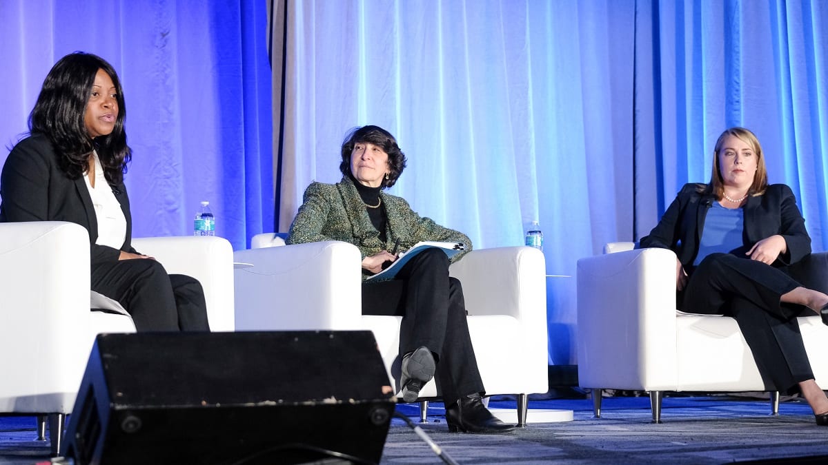 Three women sitting on a stage at a conference.