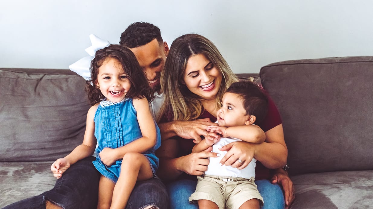 A family sits on a couch and smiles.