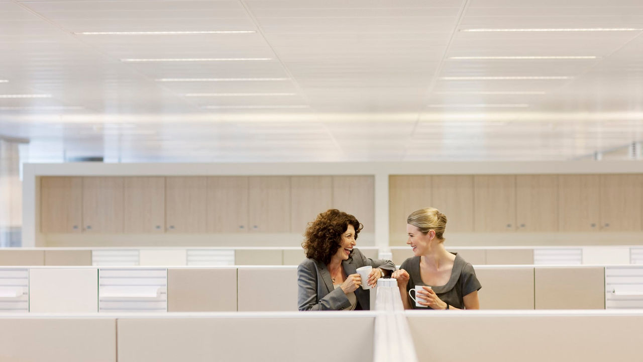 Two women talking in an office cubicle.