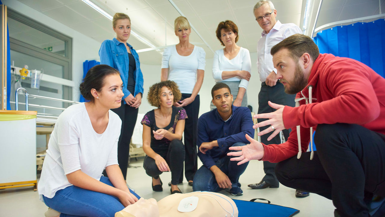 A group of people sitting around an ecg dummy.