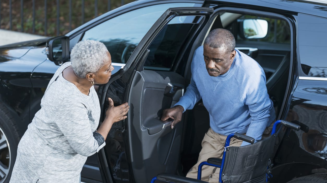 Elderly couple getting out of a car with a wheelchair.