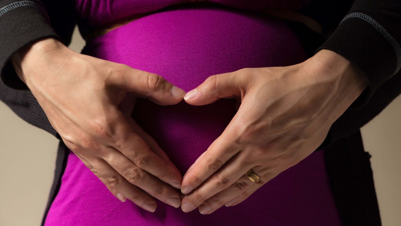 Pregnant woman making a heart shape with her hands.