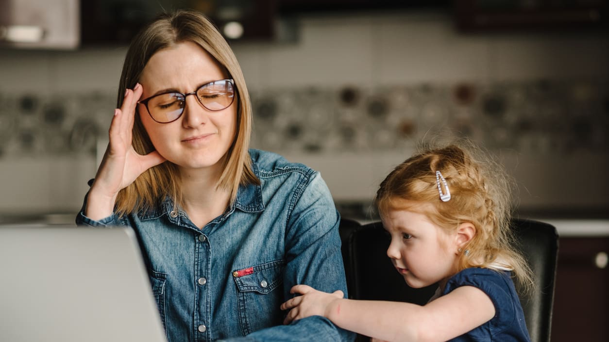 A woman is working on a laptop while her daughter is looking at it.