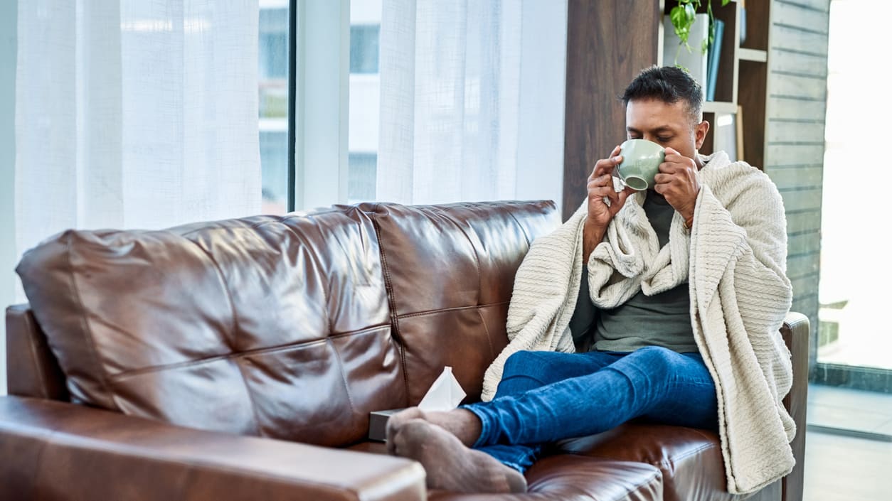 A woman sitting on a brown couch drinking a cup of coffee.