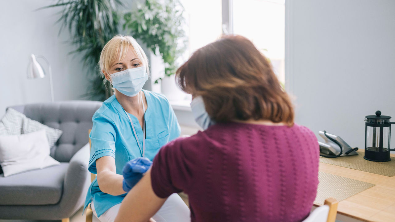 A woman wearing a face mask is giving a shot to another woman.