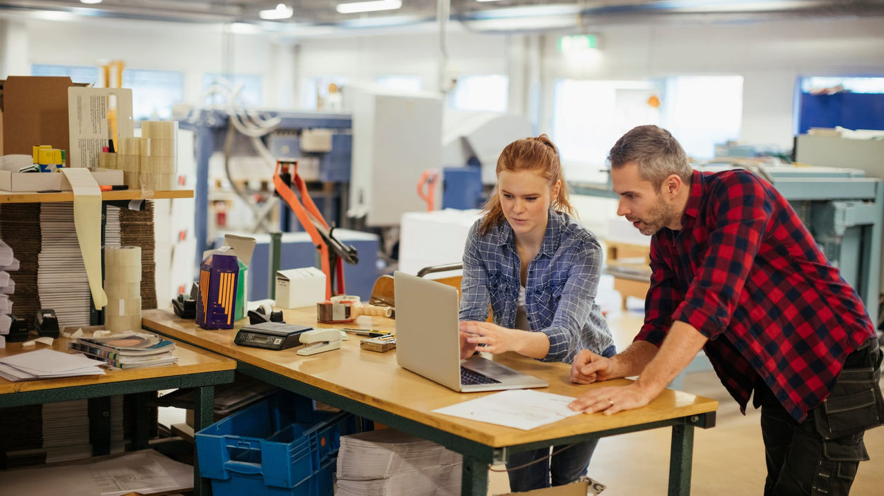 Two people working on a laptop in a factory.