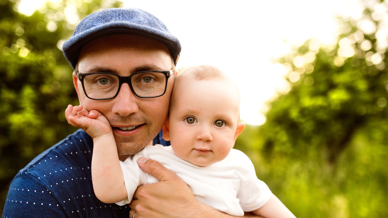 A man holding a baby in an orchard.