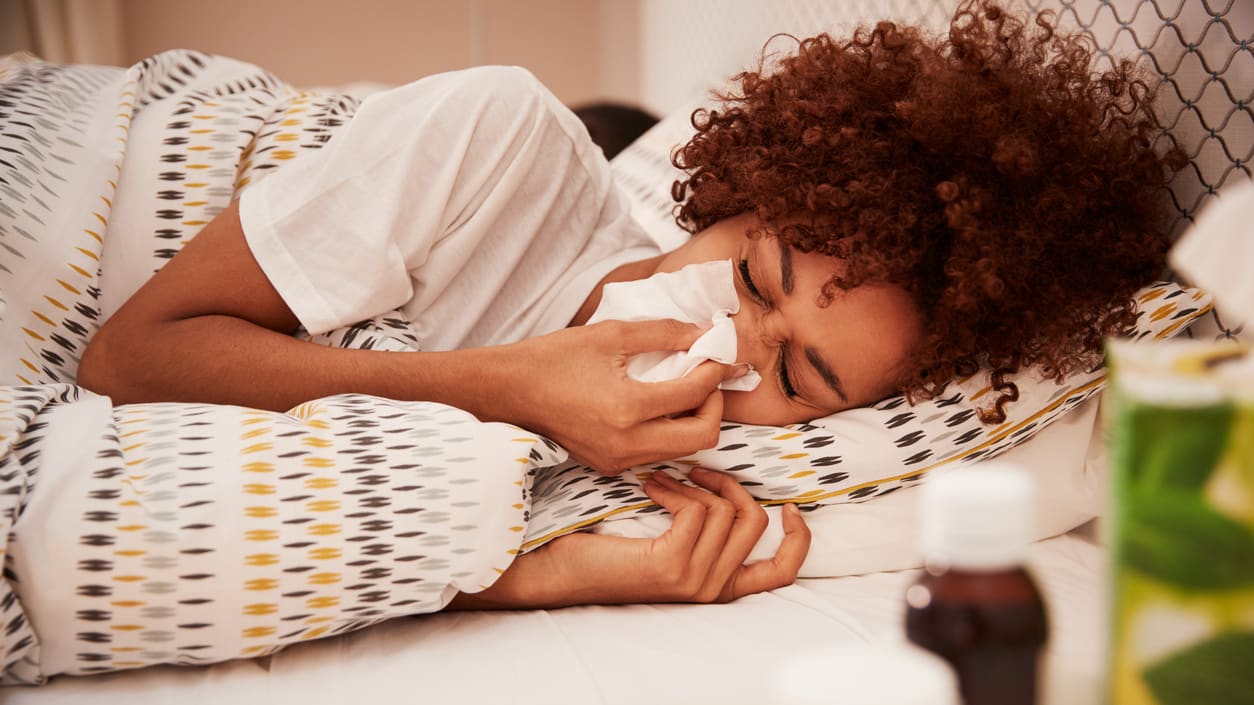 Woman sneezing and blowing her nose in bed.