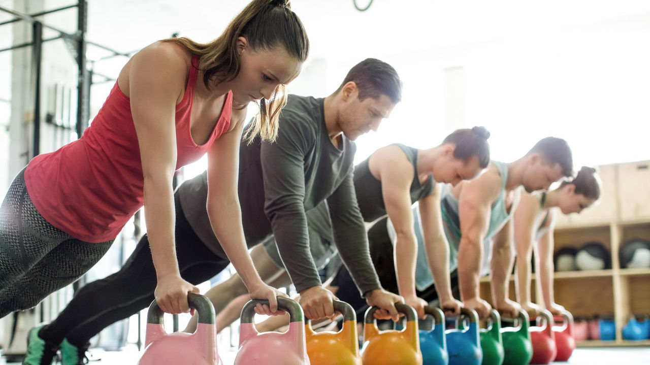 A group of people doing kettlebell exercises in a gym.