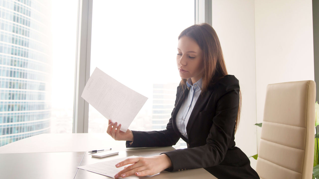 A business woman is sitting at a desk reading a document.