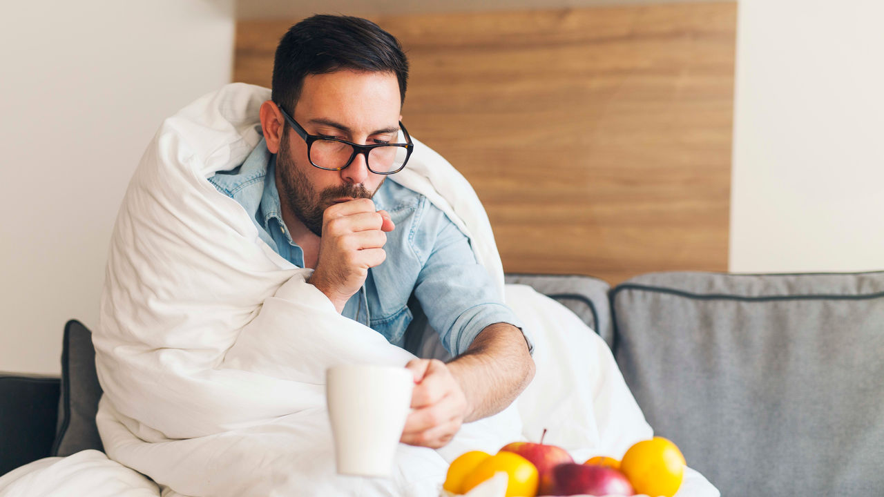 A man with a cold is sitting on a couch with a blanket.