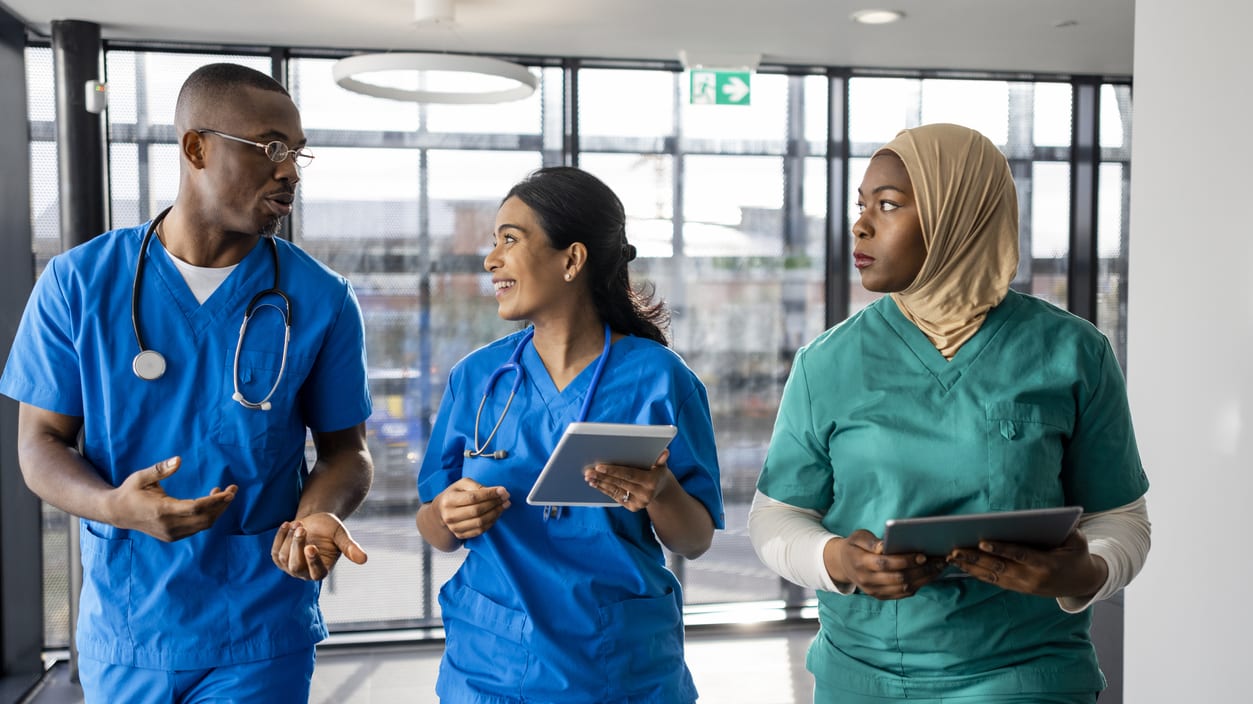 A group of nurses are walking down a hallway with a tablet in their hands.