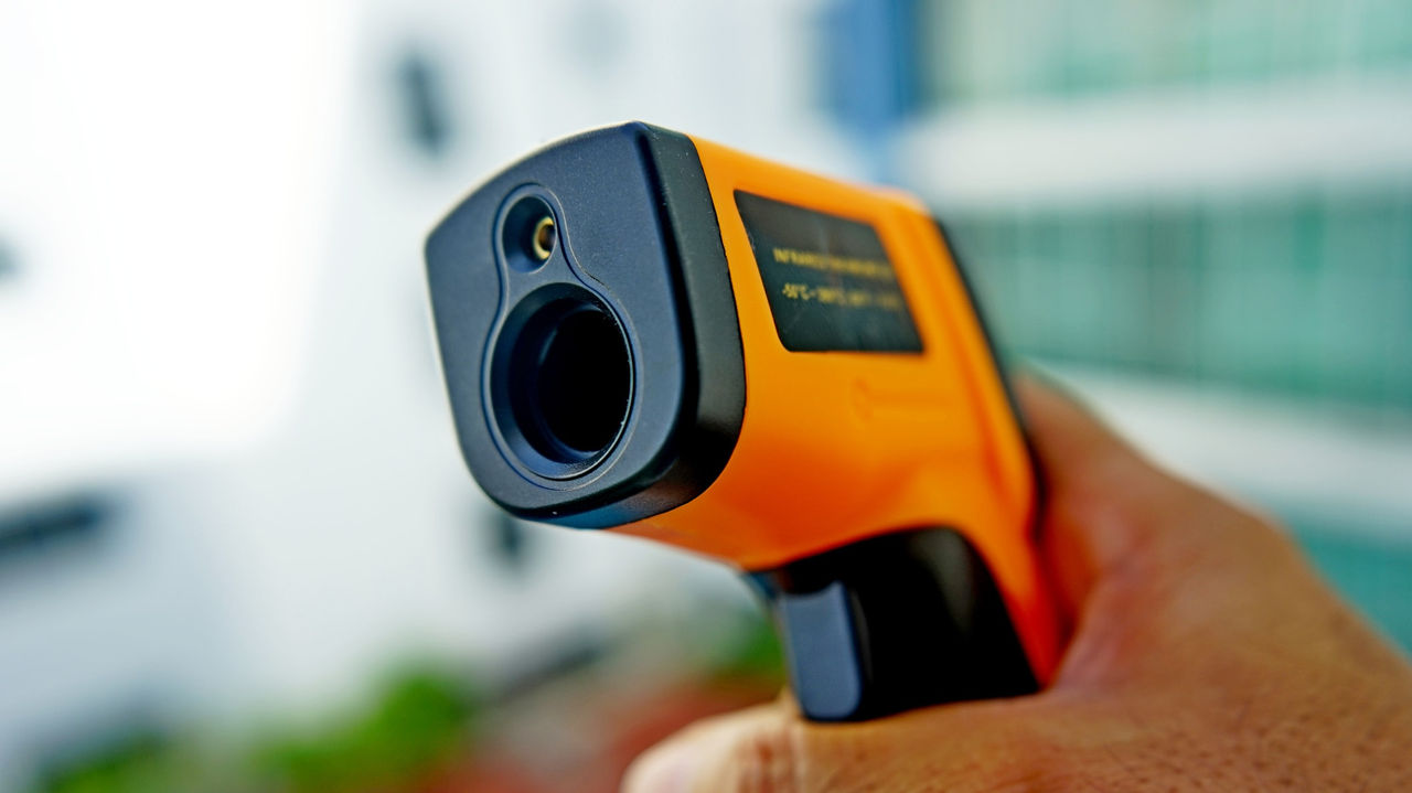 A person holding an infrared thermometer in front of a building.