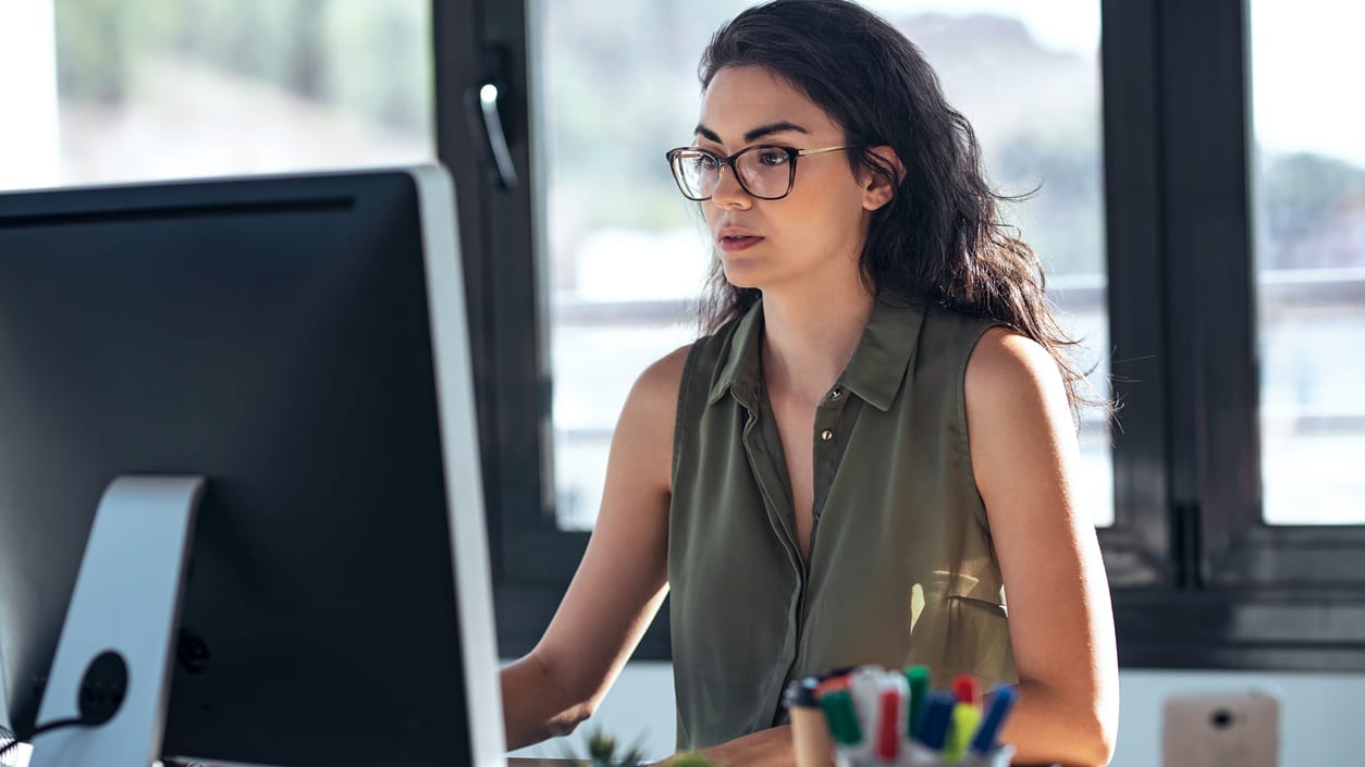 A woman wearing glasses is working on a computer.