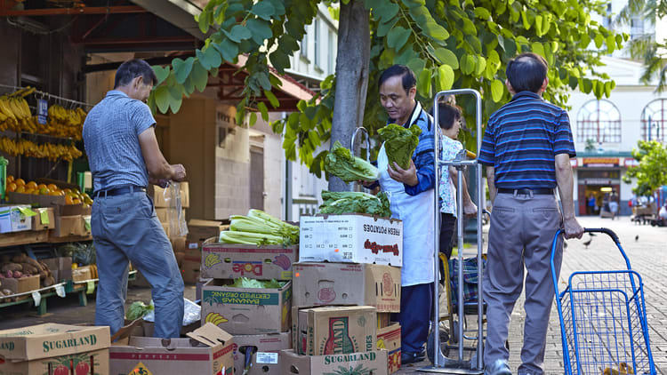 A group of men standing next to a cart full of fruit and vegetables.