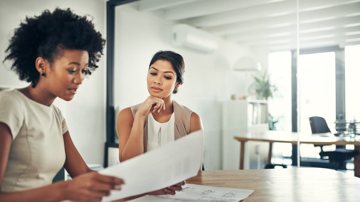 Two business women talking at a table in an office.