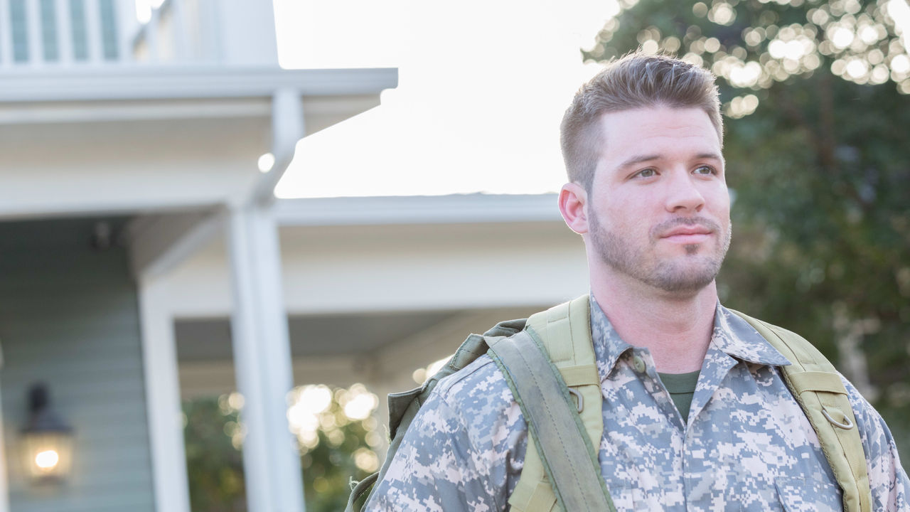 A man in camouflage standing in front of a house.