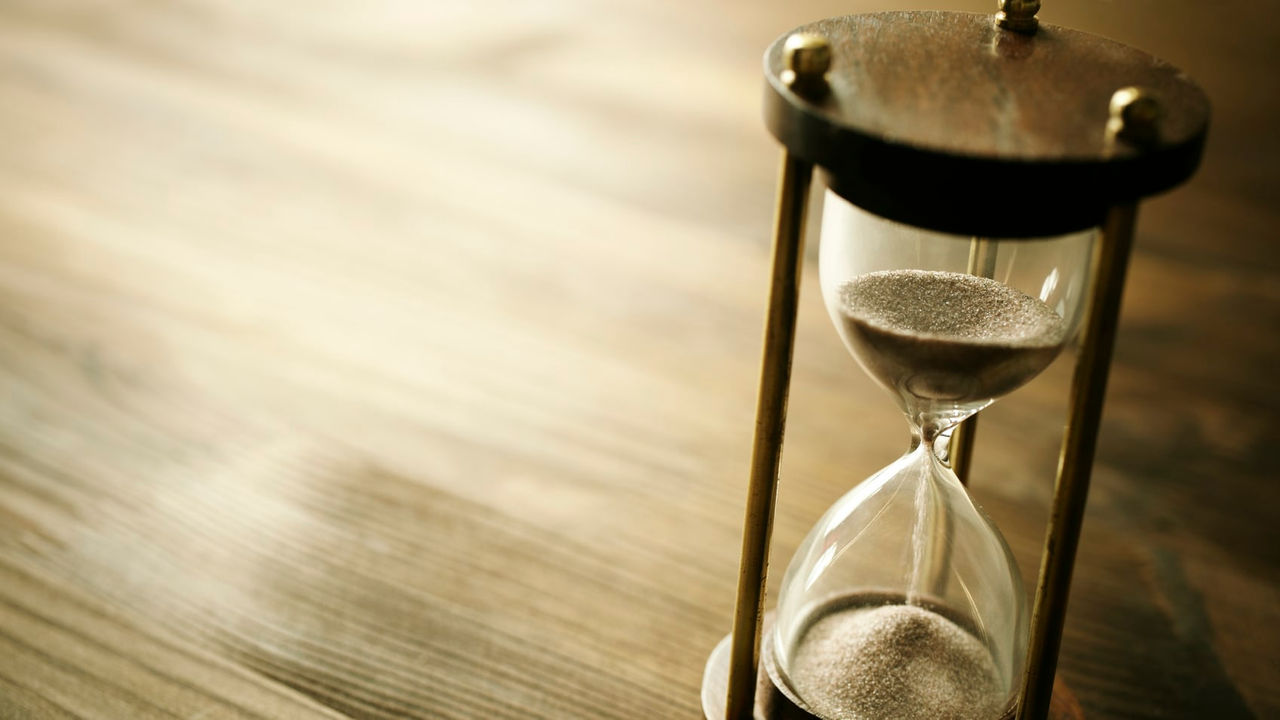 A sand hourglass sitting on a wooden table.