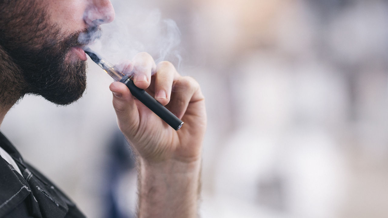 A man with a beard smoking an electronic cigarette.