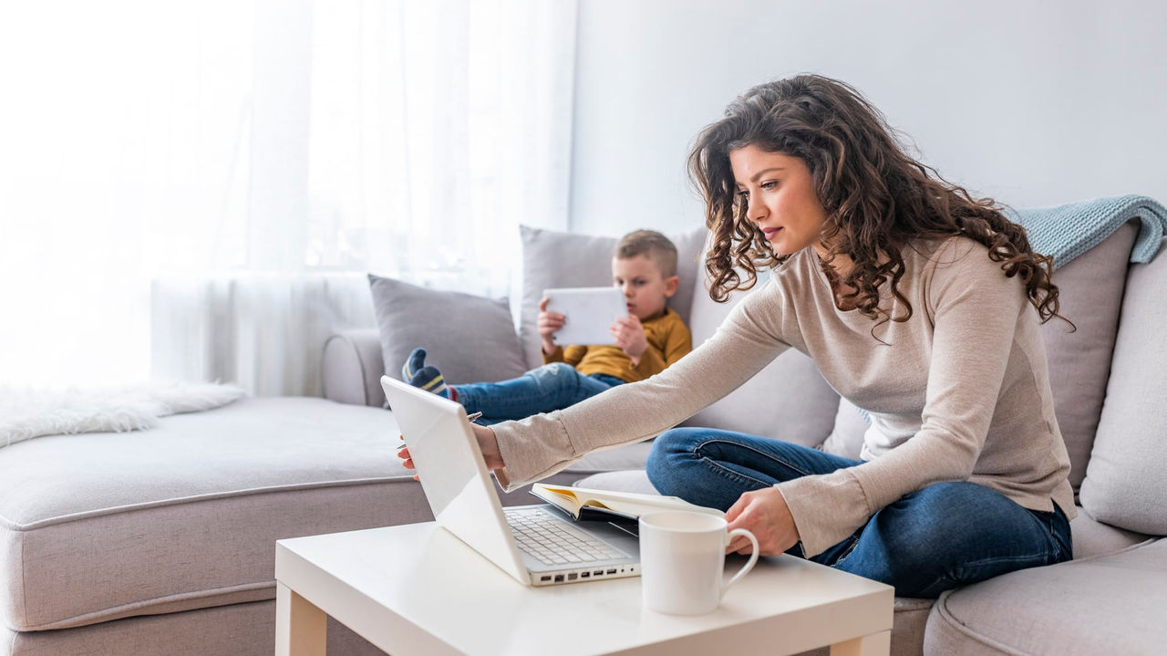 A woman sitting on a couch with her son using a laptop.