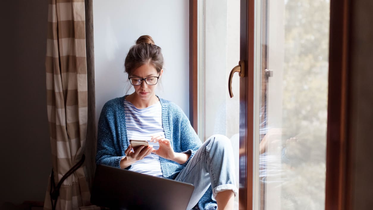 A woman sitting on a window sill using her laptop.