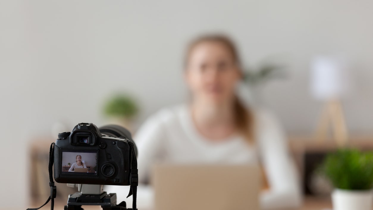 A woman is sitting in front of a video camera in front of a laptop.