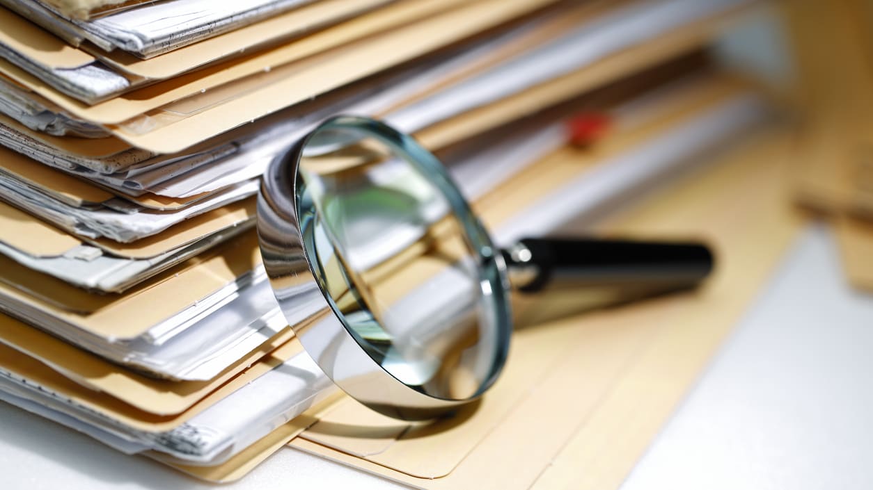 A magnifying glass sits on top of a stack of files.