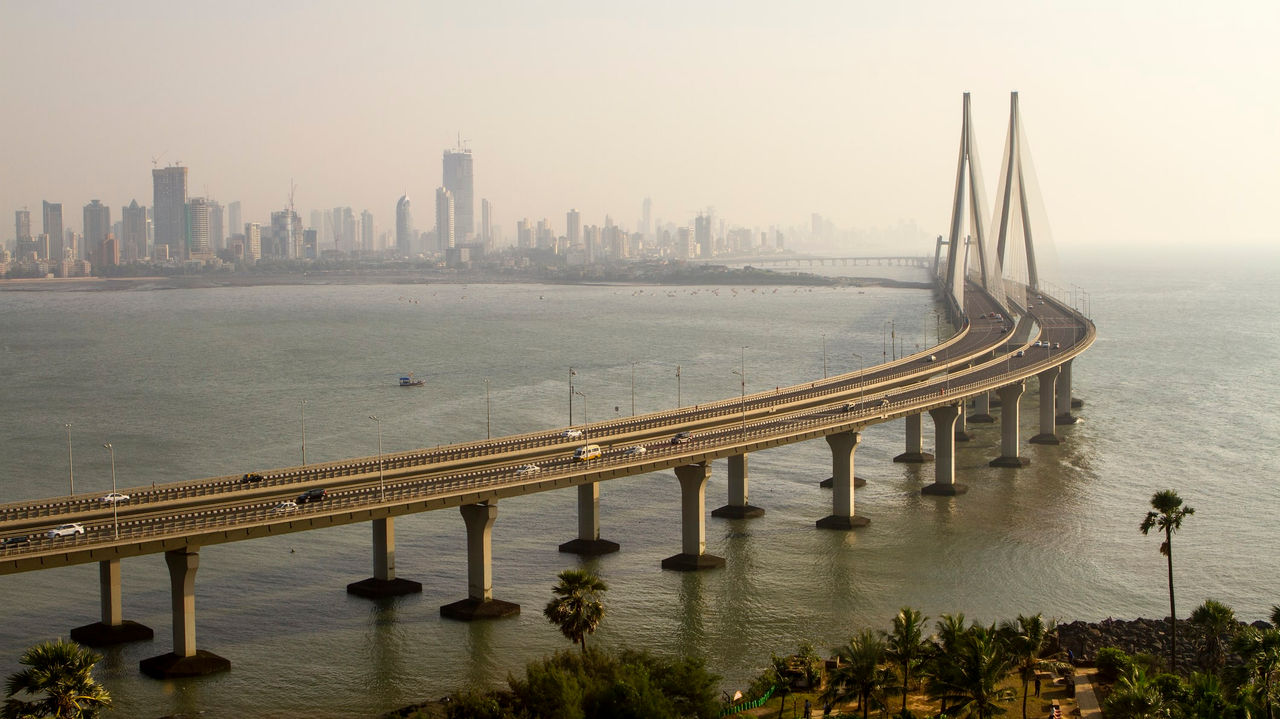 A long bridge spanning the water with a city in the background.