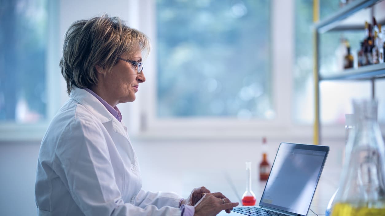 A woman in a lab coat using a laptop.