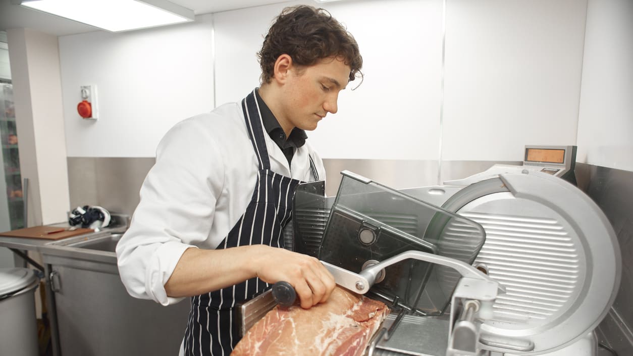 A man is slicing a piece of meat in a kitchen.