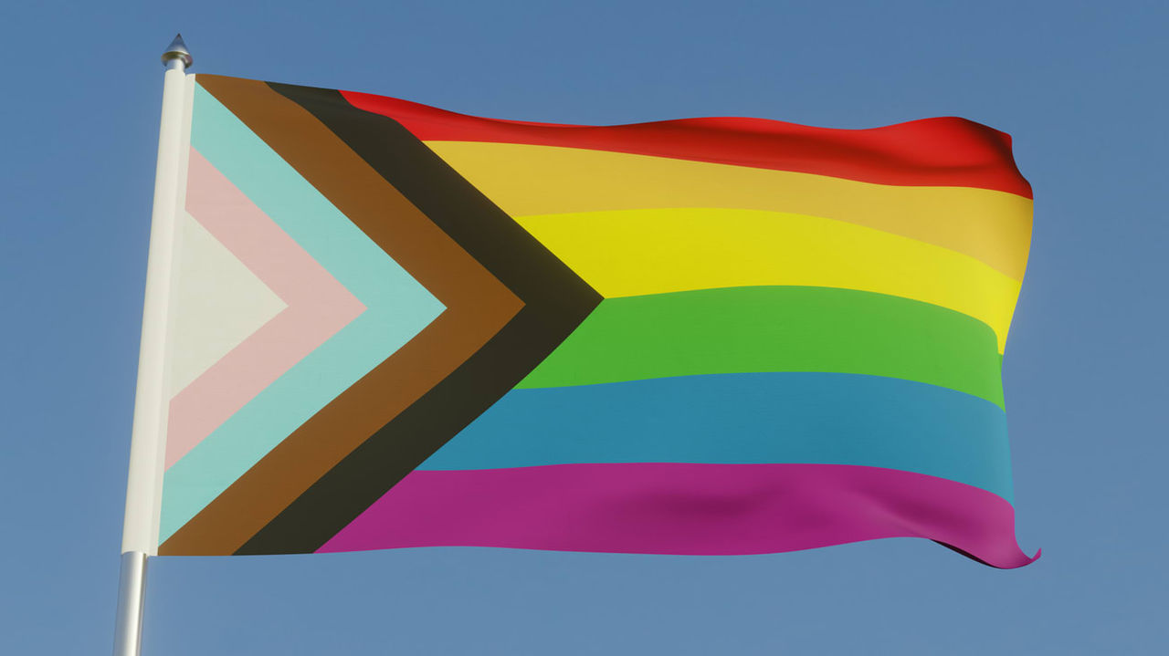 A rainbow flag flying in the air against a blue sky.