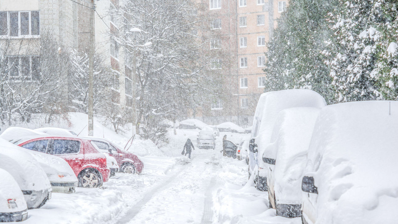 A snow covered street with cars parked in it.