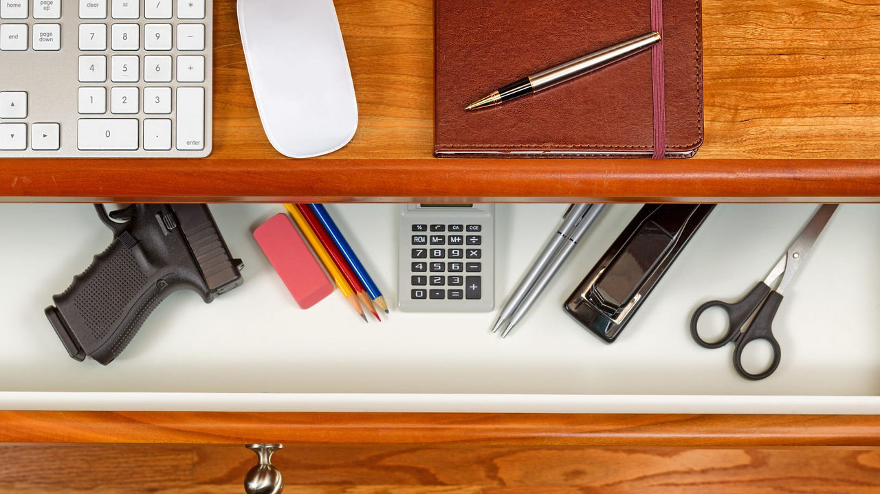 A desk with pens, pencils, a calculator and a gun.
